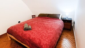 Quarto com cama, mesa de cabeceira, luminária e cadeira.