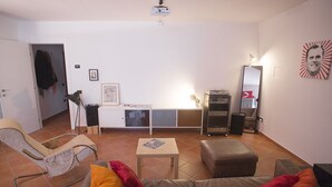 Uma sala de estar com sofá, poltrona, mesa pequena, armário, espelho e projetor de teto.
