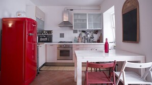 Cozinha compacta com geladeira vermelha, armários brancos, fogão a gás e um pequeno espaço de jantar com mesa branca e duas cadeiras.