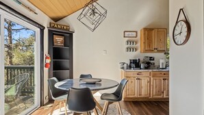 Une cuisine chaleureuse avec des meubles de rangement en bois, une table de salle à manger ronde entourée de chaises, un luminaire suspendu et une horloge au mur.
