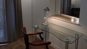 Een kamer met een glazen tafel, een houten stoel, een lamp en een spiegel aan de muur.