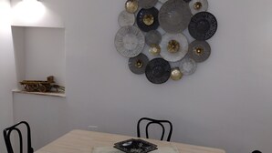 Een eetruimte met een lichte houten tafel, vier zwarte stoelen, een decoratief wandobject en een klein plankje met een model.