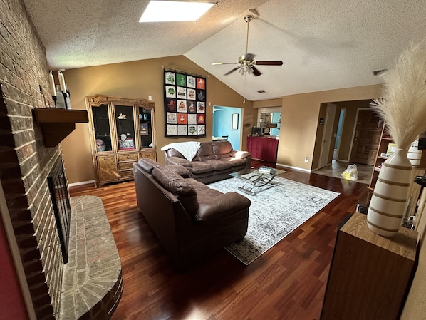 A spacious living room with a fireplace, a ceiling fan, and a large rug.