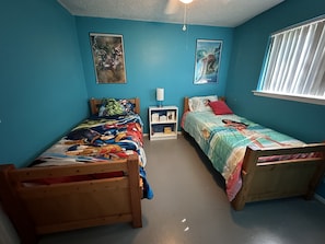 A bedroom with two wooden beds, teal walls, and two framed posters.