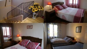 A hotel room with a wooden staircase, a bed with red and white bedding, a nightstand with a lamp, and a window with curtains. - Maison DE Village (Formiguères)