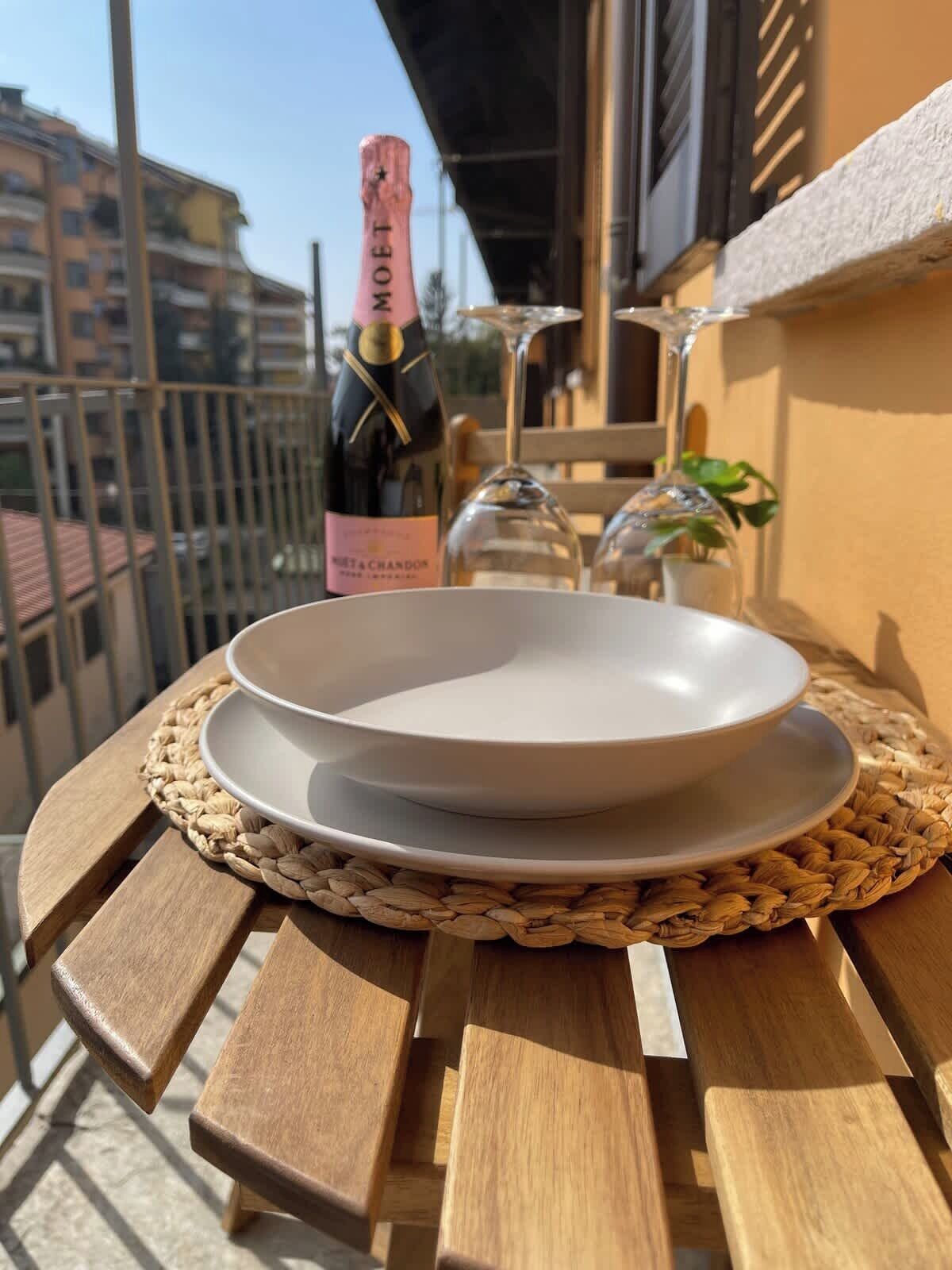 A balcony with a wooden table, a white plate, a wine bottle, and two glasses.