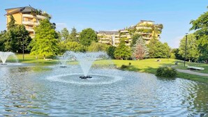 Un parque tranquilo con una fuente, abundante vegetación y edificios residenciales al fondo.