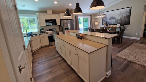 A modern kitchen with a central island, stainless steel appliances, pendant lighting, and a dining area with a view of the outdoors. - Rainforest Getaway - Hot tub, bar, game room, creek in Forks...relax in style! (Forks)