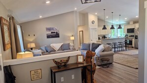 A modern living room with a sofa, a coffee table, and a dining area with bar stools. - Rainforest Getaway - Hot tub, bar, game room, creek in Forks...relax in style! (Forks)
