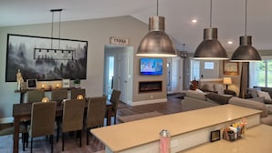 A modern kitchen with a central island, pendant lighting, and a dining area with chairs and a table. - Rainforest Getaway - Hot tub, bar, game room, creek in Forks...relax in style! (Forks)