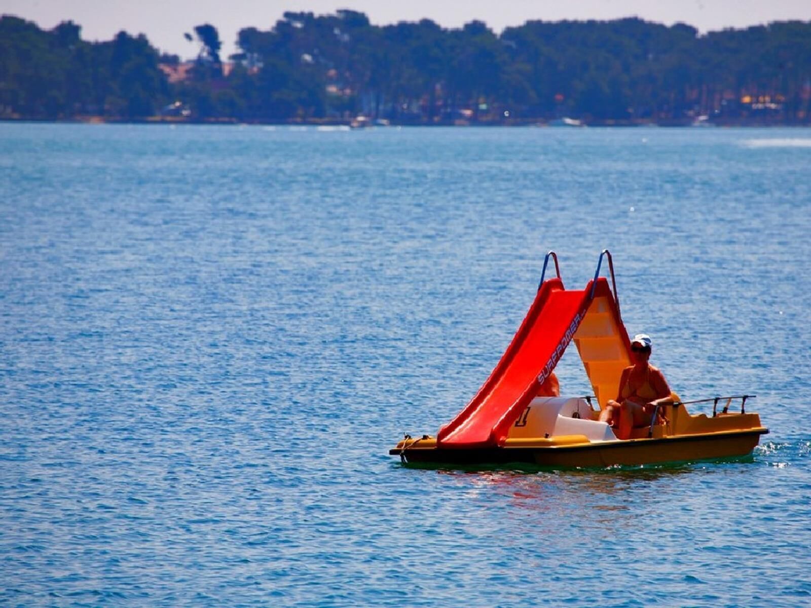 A small yellow boat with a red canopy on a calm body of water.