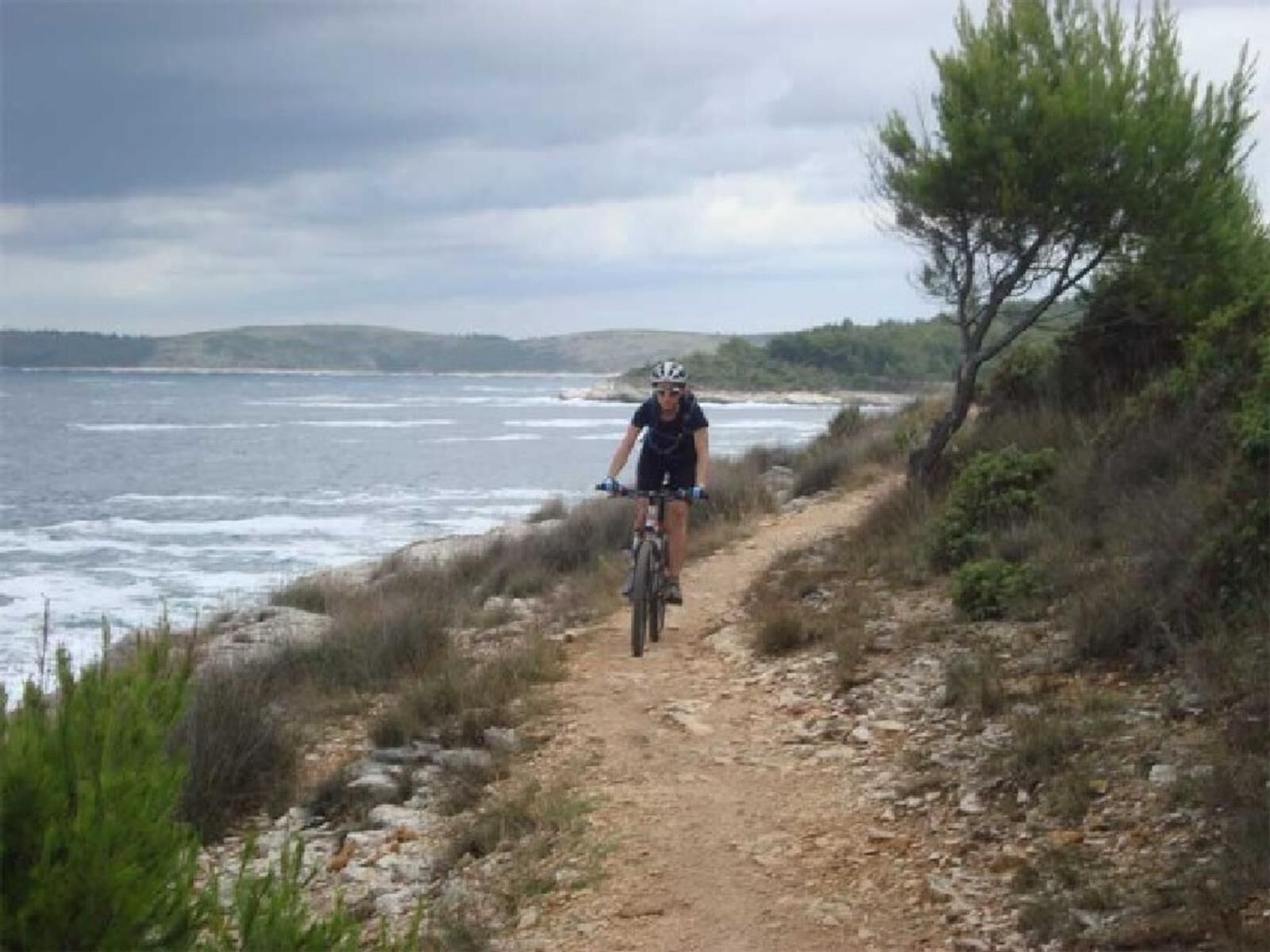 A person riding a bicycle on a rocky coastal path with the sea in the background.
