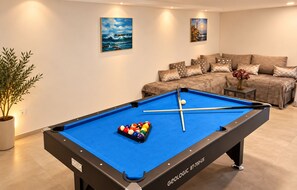 A pool table with balls, a sofa set, and two paintings on the wall.