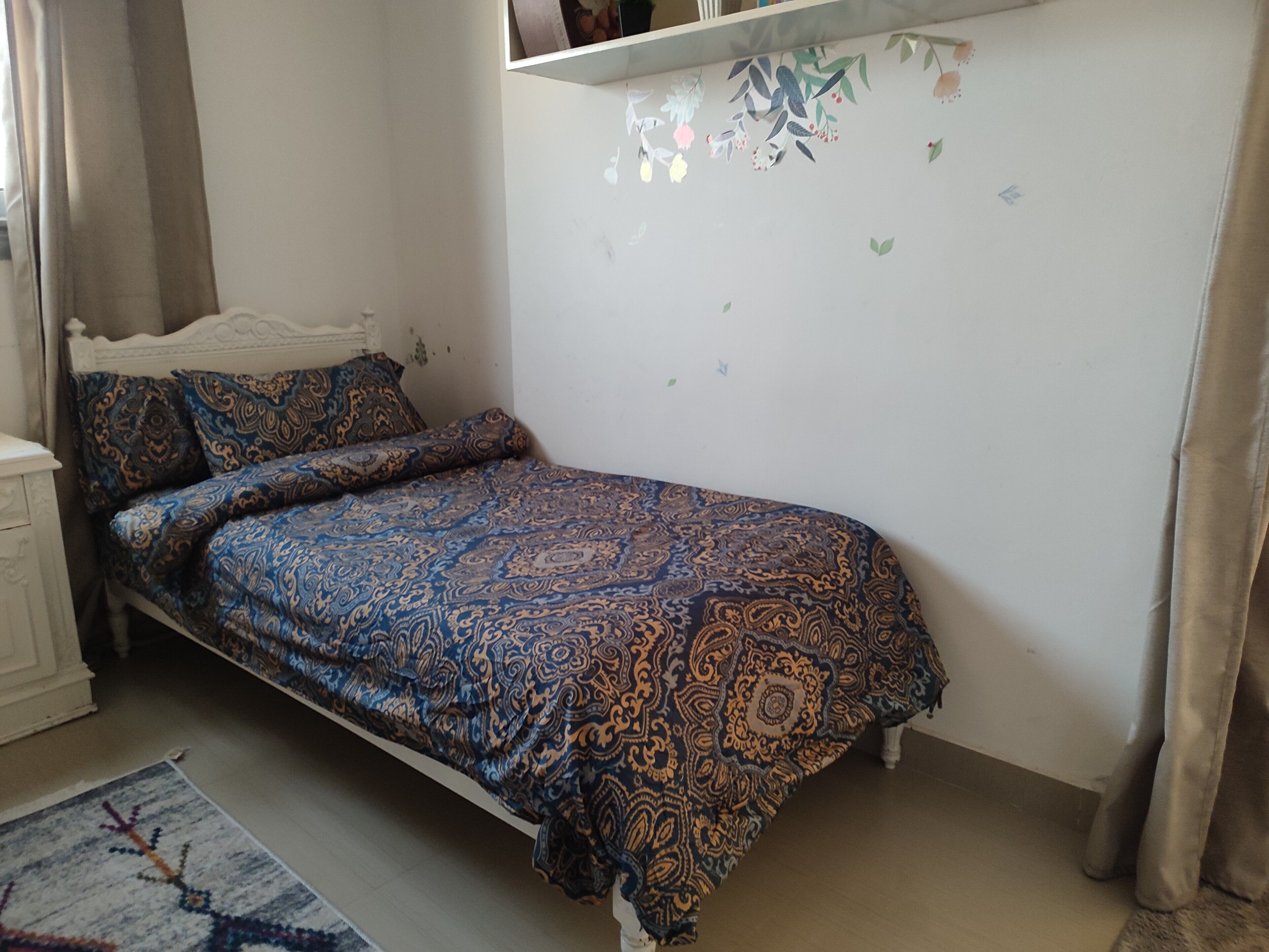 A bedroom with a bed, a nightstand, and a wall with a floral pattern.