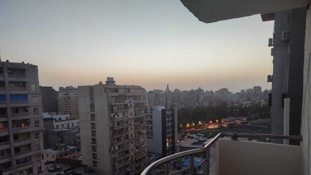 Un immeuble de grande hauteur doté de nombreux balcons, offrant une vue sur le paysage urbain, avec un coucher de soleil en arrière-plan.