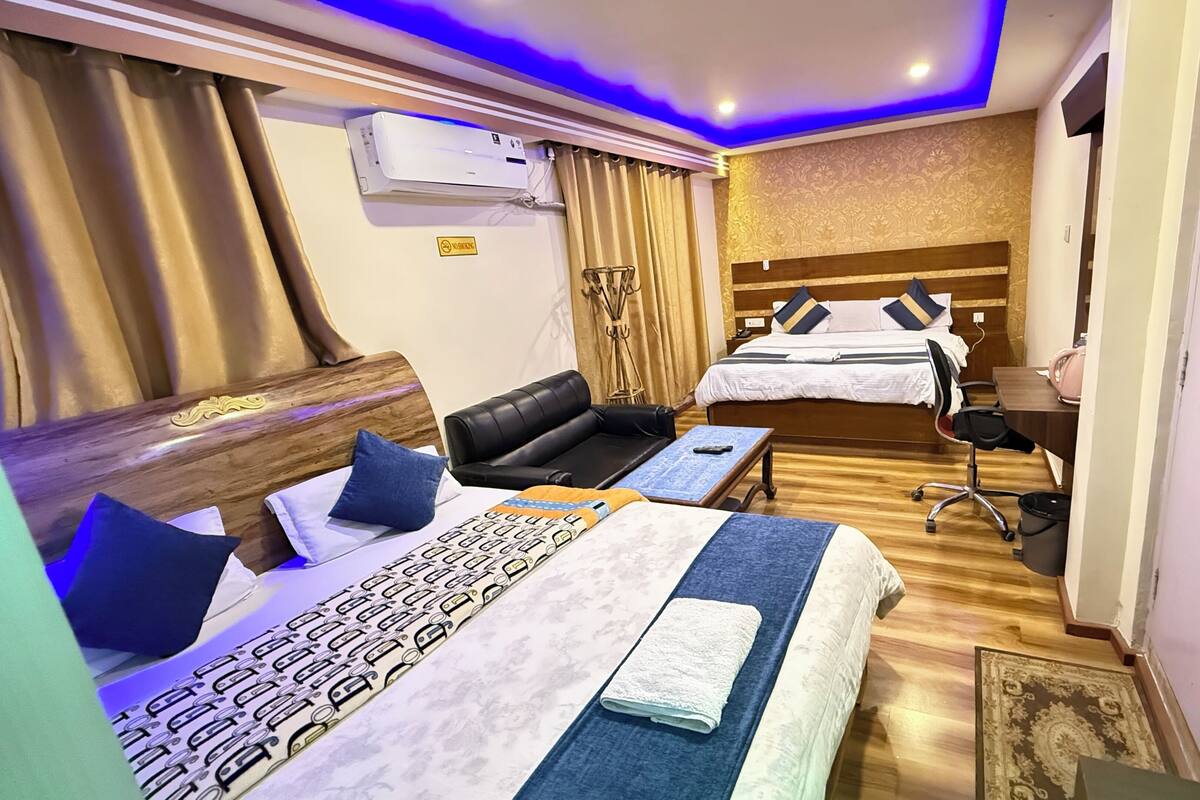 Habitación de hotel con dos camas, un escritorio, una silla, un sofá y un aire acondicionado.