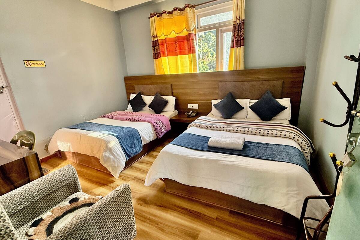 Una habitación con dos camas, piso de madera, una mesa y una silla.