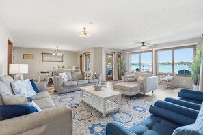 A spacious living room with a large window offering a view of the sea, a dining area with a table and chairs, and a seating area with sofas and a coffee table. - 4BR Lakefront · Pier · Game Room · Sleeps 16+ (North Webster)