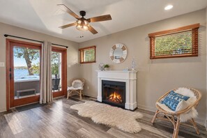 A room with a fireplace, a ceiling fan, and a view through a glass door. - 4BR Lakefront · Pier · Game Room · Sleeps 16+ (North Webster)