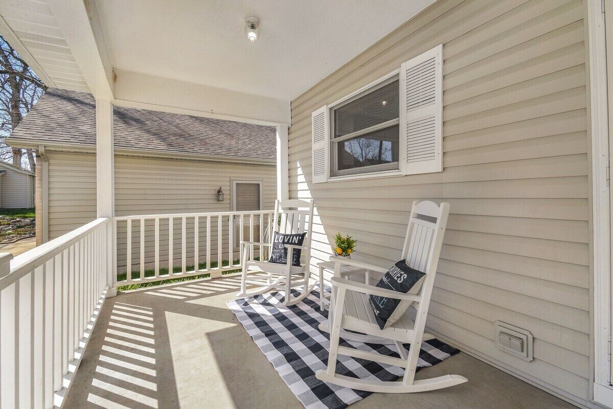 A porch with a rocking chair and a small table, a window with shutters, and a white railing.