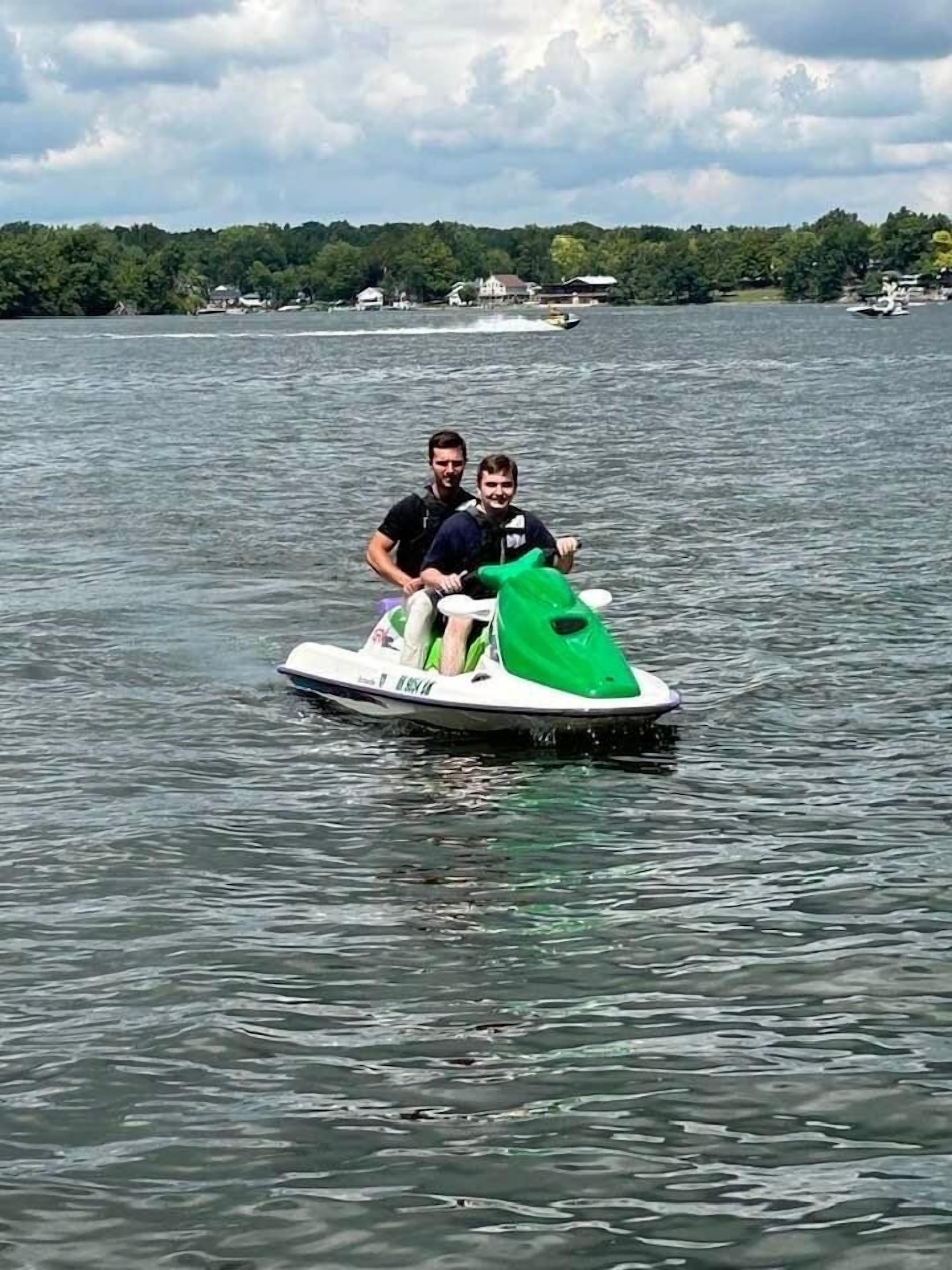Dos personas en un jet ski verde y blanco en un lago, con casas al fondo.