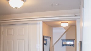 A hallway with a white door, wooden flooring, and a staircase leading to another room.