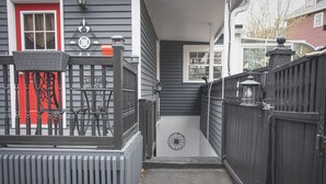 A narrow outdoor pathway leading to a house with a red door, a small porch, and a black gate.