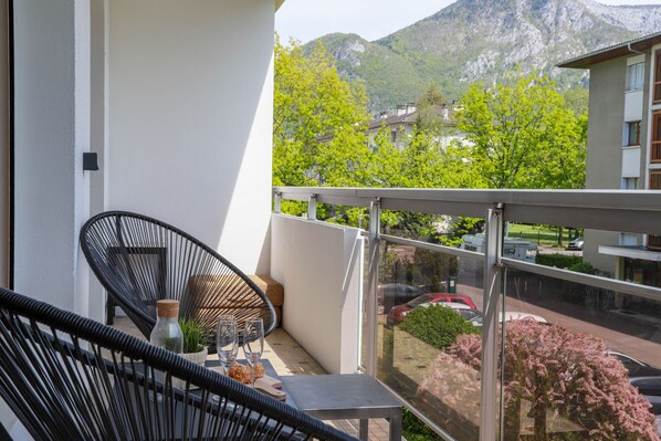 Un balcon avec une chaise en osier, une petite table et une bouteille.