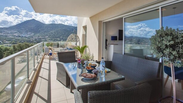 A balcony with a table set for breakfast, wicker furniture, and a view of mountains.