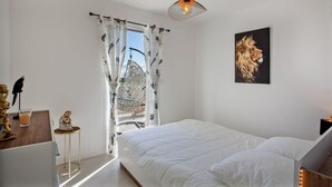 A bedroom with a bed, a window with curtains, a hanging light fixture, and a wall-mounted painting.