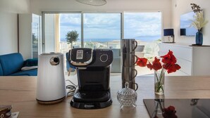 A modern kitchen with a coffee maker, a kettle, and a vase with red flowers on a wooden table.