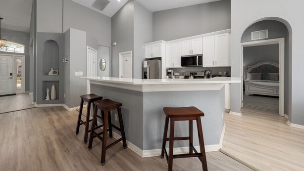 Una cocina moderna con una isla grande, armarios blancos y taburetes de madera.