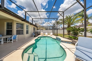 A pool area with a clear view of the sky, a pool, lounge chairs, and a covered patio.