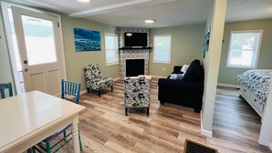A cozy living room with a fireplace, a sofa, a dining table, and a TV mounted on the wall.