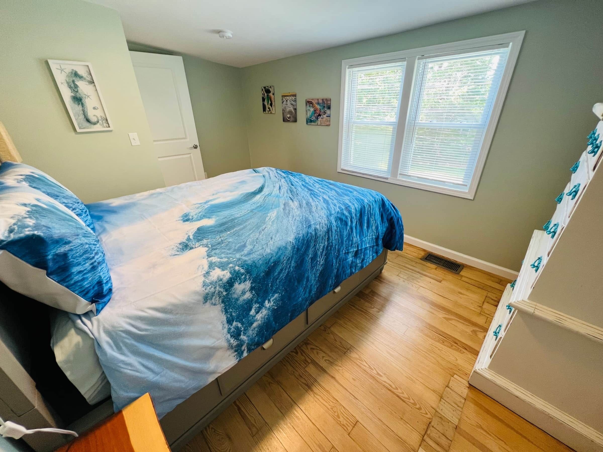 Un dormitorio con cama, ventana con persianas, puerta y una pared con tres cuadros pequeños.