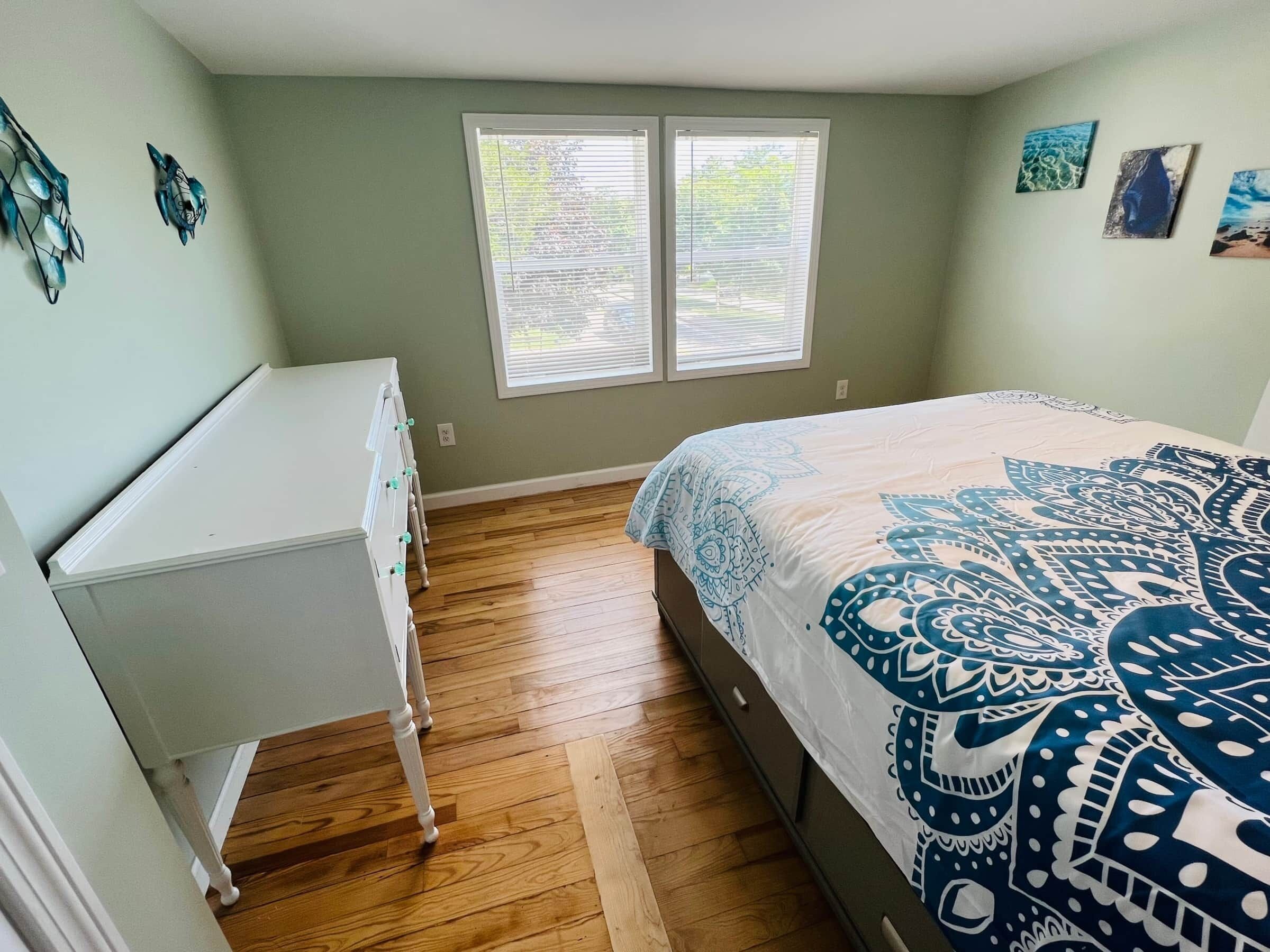 A bedroom with a bed, a dresser, a window, and artwork on the walls.