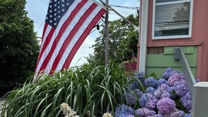 A house with a large American flag, a mailbox, and a variety of flowers including hydrangeas and white flowers.