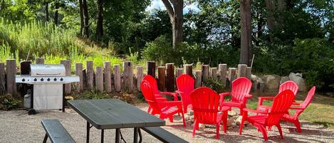 An outdoor patio with a grill, picnic table, and red chairs.