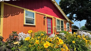 A red house with a yellow trim and a red door, surrounded by yellow flowers and greenery. - Plymouth MA White Horse Beach Moana (Plymouth)