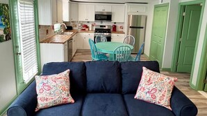 A modern kitchen with white cabinets, a dining area with a teal table and chairs, and a dark blue sofa with patterned cushions. - Plymouth MA White Horse Beach Moana (Plymouth)