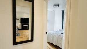 Ein Flur, der zu einem Schlafzimmer mit einem Bett, einem Spiegel und einer Deckenleuchte führt.