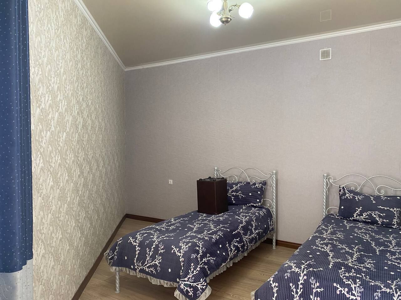 A bedroom with two beds, a ceiling light, and a wall-mounted heater.