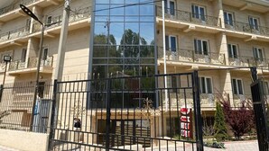 Un hotel de varios pisos con fachada central de vidrio, balcones con barandillas de hierro forjado y una entrada protegida por un portón.
