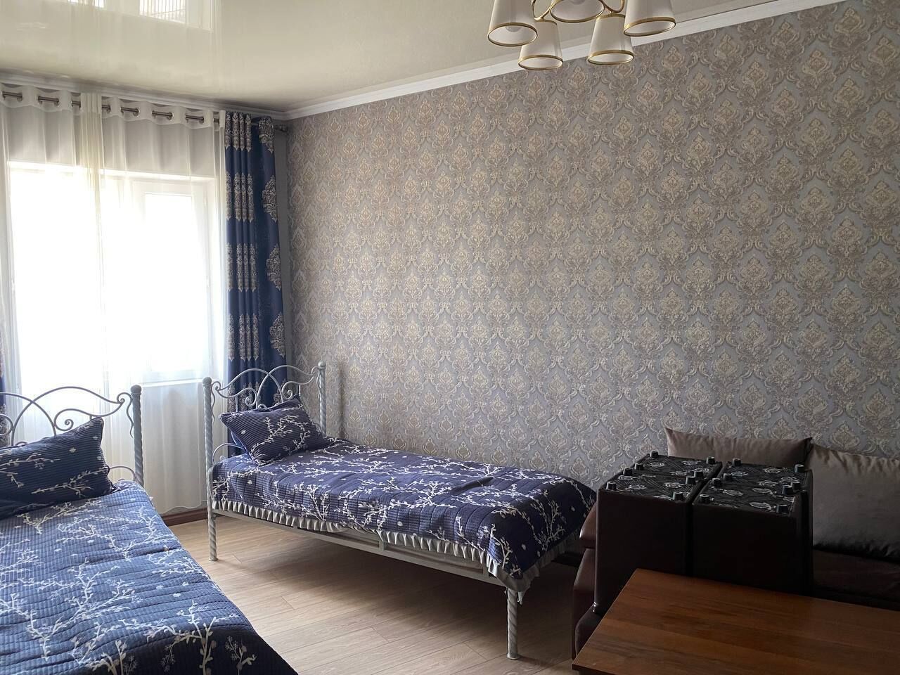 Un dormitorio con dos camas de metal, papel tapiz estampado y suelo de madera.