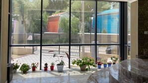 Una habitación amplia con ventanas grandes, suelo de baldosas y varias plantas en macetas.