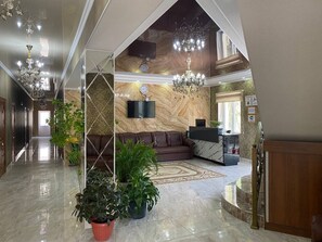 A spacious lobby with a marble floor, a leather sofa, a chandelier, and potted plants.