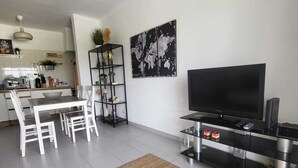 Een moderne woonkamer met een eethoek, een flatscreen-tv en een keuken op de achtergrond.
