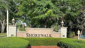 Un panneau indiquant le nom « Shorewalk », entouré de haies bien entretenues et bordé d’un chemin de pierres.