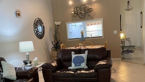 Un salon avec un canapé en cuir marron, une table basse en verre et un tapis à motifs.