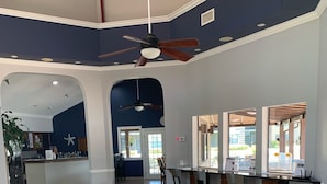 Un intérieur spacieux avec un plafond haut, un espace salon central avec des fauteuils et une table, et une cuisine ouverte sur le reste de la pièce par une arche.
